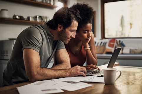 Couple at kitchen counter reviewing finances and applying for a HELOC on open laptop.