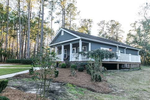 Blue manufactured home with wrap around porch in wooded lot.