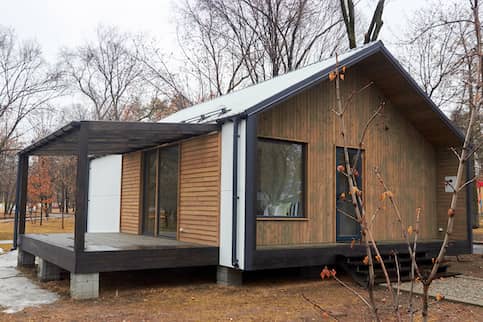 Modular home with covered porch and wood siding in a wooded lot.