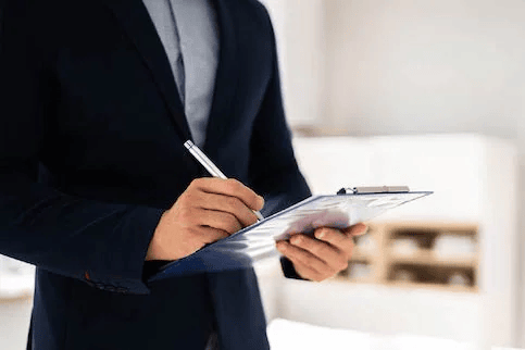 Man in dark blazer writing on clipboard.