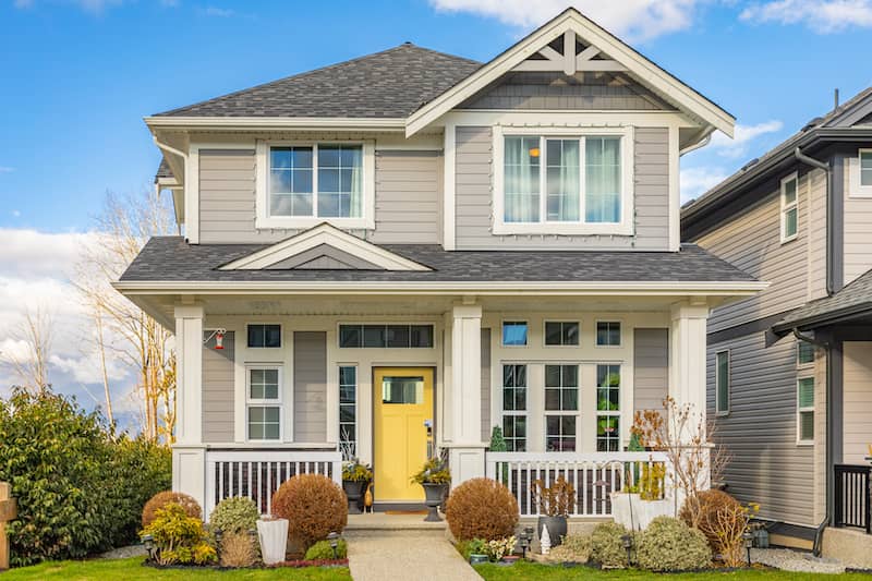 Gray two-story home without-white trim and yellow door.