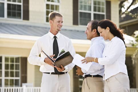 Couple talking to a real estate agent in front of a house.