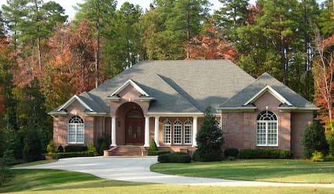 Large modern brick home with long winding drive way surrounded by large trees in Autumn.