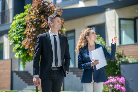 Female real estate agent walking outside with man in suit showing him condos.