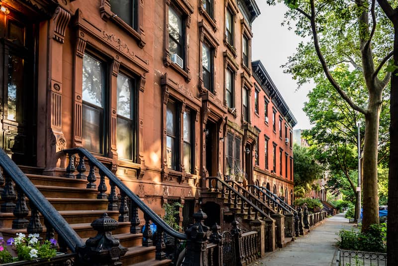 Classic Brooklyn brownstone block with a long facade and ornate stoop balustrades on a summer day in Clinton Hills, Brooklyn