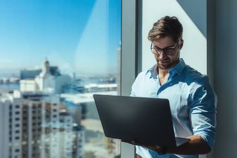 Business investor standing by a window holding a laptop