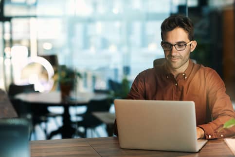 Young professional man in brown shirt working on laptop at table in office.