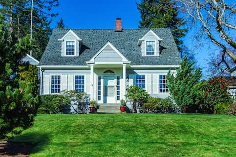 Gray Cape Cod Style home with a small yard with rose bushes.