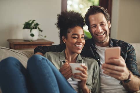 Couple looking at phones together on couch in home with houseplants.