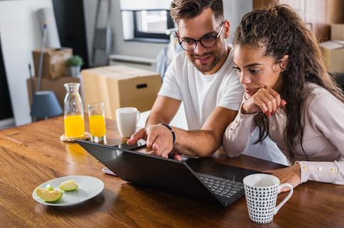 Couple looking online at homes with boxes packed up in background.