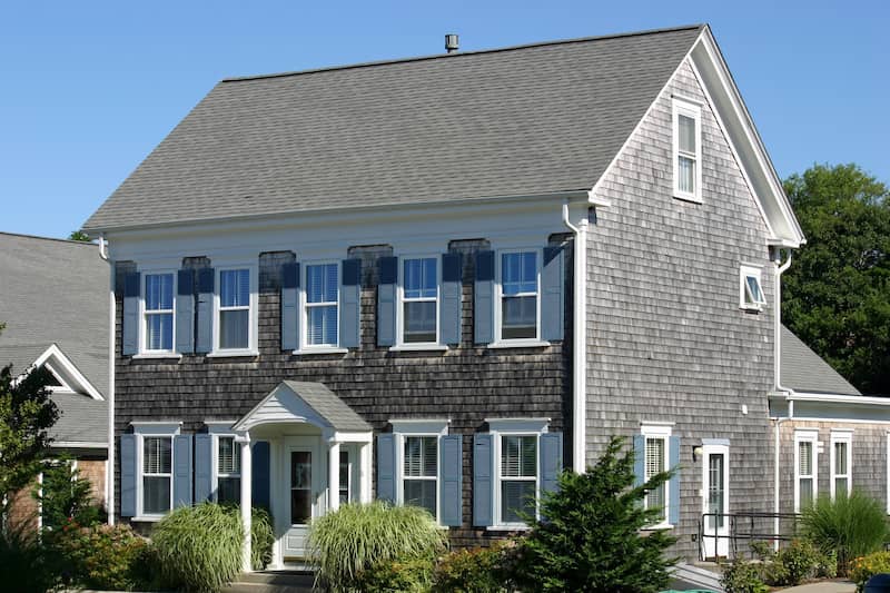 Large classic Cape Cod style home with grey shingles and two floors plus attic.