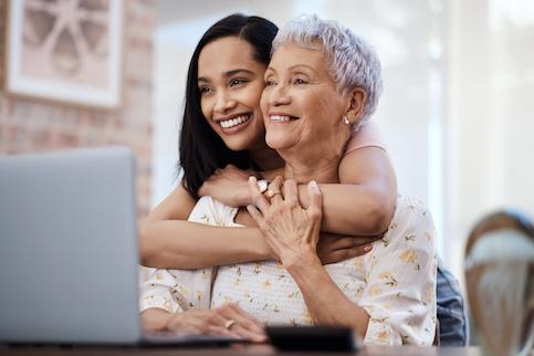 Grandmother on laptop and grand daughter is embracing her from behind.