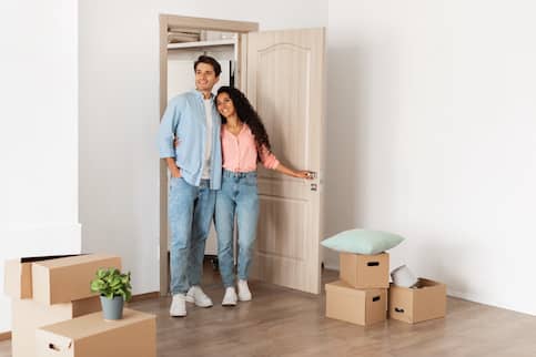 Young, happy couple, walking into room of new home, filled with moving boxes