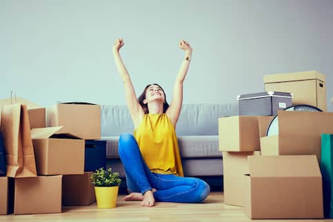 Happy young woman sitting on the floor amongst moving boxes.