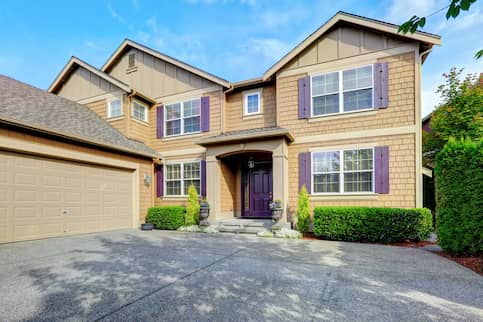 Large, two-story tan house with purple shutters and door.