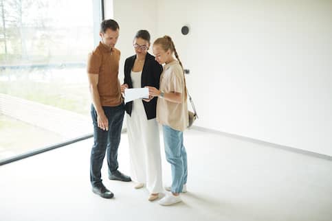 Man and two women standing in an empty house reviewing a paper document.