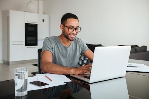 Happy young man using laptop at home to check his finances.