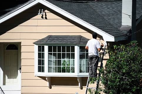 Man standing on ladder exterior siding of home. 