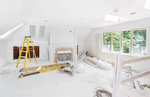 Large white room under construction with two yellow ladders, taped off fireplace and scattered tools.