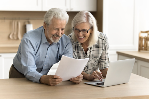 Senior couple smiling as they look at paperwork for a refinance approval.