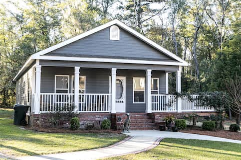 Blue manufactured home, with white railings, windows and a door, with a garden in the front yard.