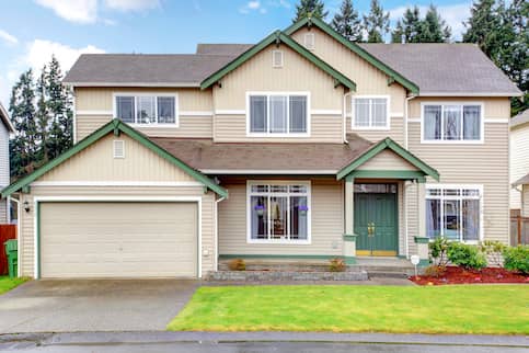 Traditional, two-story house with two-car garage, green door, tan siding and green and beige trim.