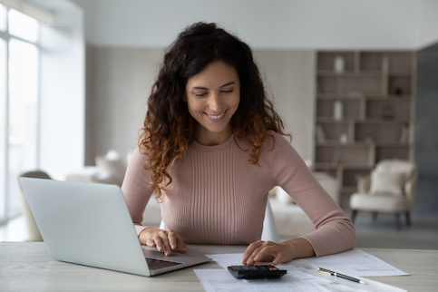 Woman at home office desk smiling calculating finances.