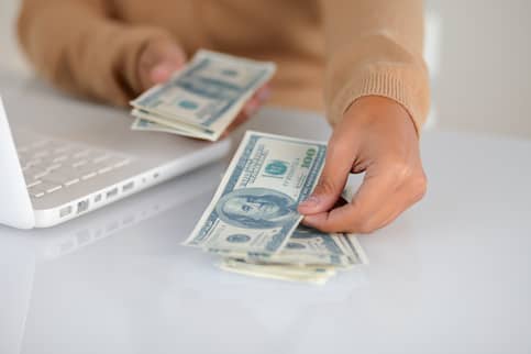 Close-up of womanu2019s hands as she counts out $100 bills.