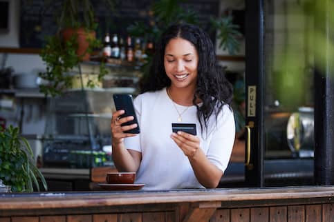 Woman in a white t-shirt holding a cell phone and credit card while sitting in a coffee shop