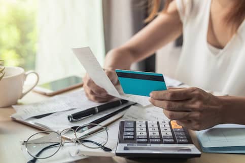 Young woman reviewing finance documents and calculating credit card expenses.