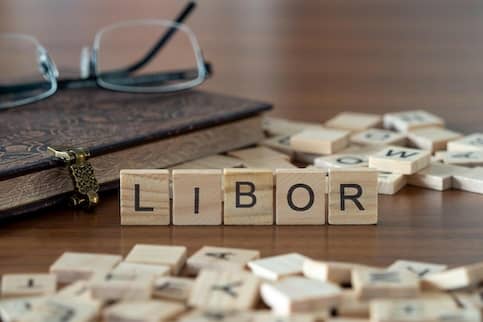 Scrabble tiles piled on a table with a pair of glasses and a book, with five tiles spelling out the letters 'LIBOR'.