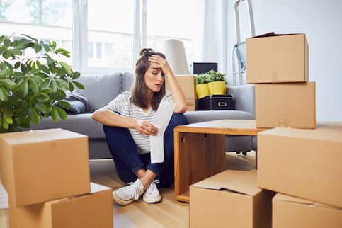 Worried Young Woman Looking At Bill Sitting On Floor After Moving In