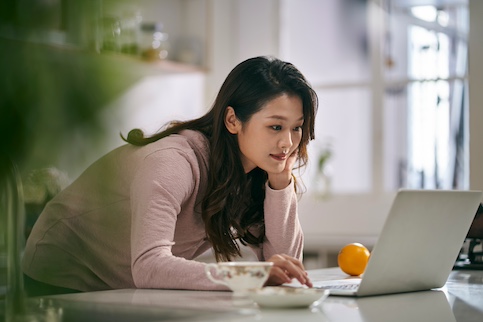 Young woman leaning over a table and using a laptop.