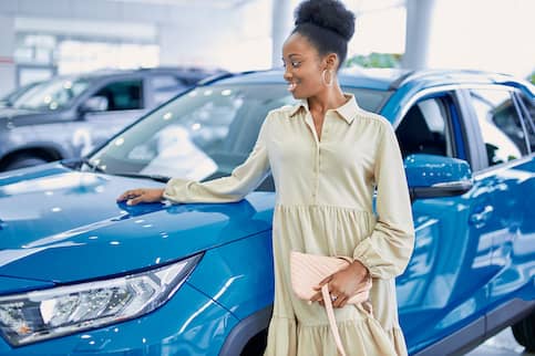 Young woman looking at a blue car in a dealership.
