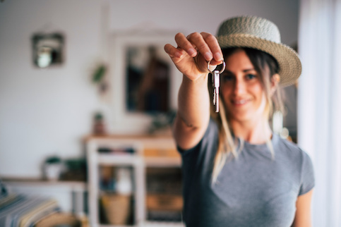 Young woman holding up house keys happily toward the photographer.