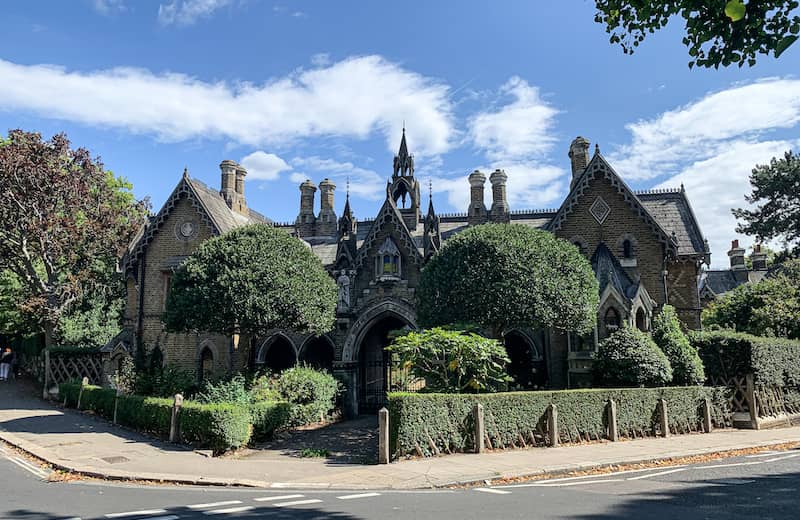 Dark, brick Gothic revival home with pointed arches, steep roofs and dark green landscaping. 