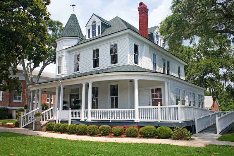 White folk Victorian home with wrap-around porch with spindles and wheelchair ramp.