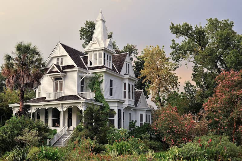 White Queen Anne home with three floors and ornate trim surrounded by trees.