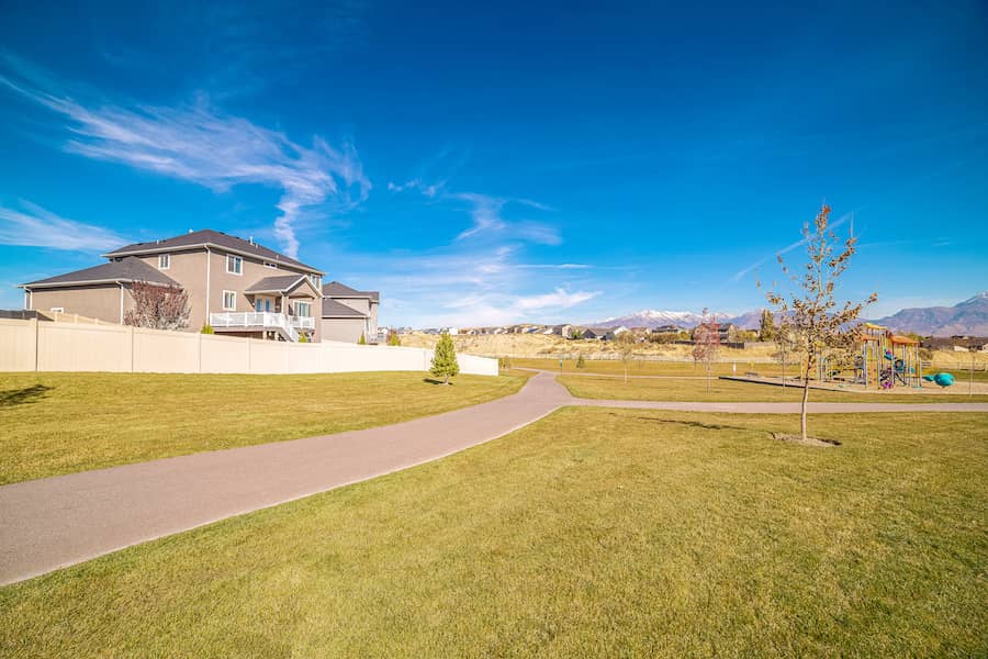 alking path cutting through grass field and playground with houses and mountains in the background.