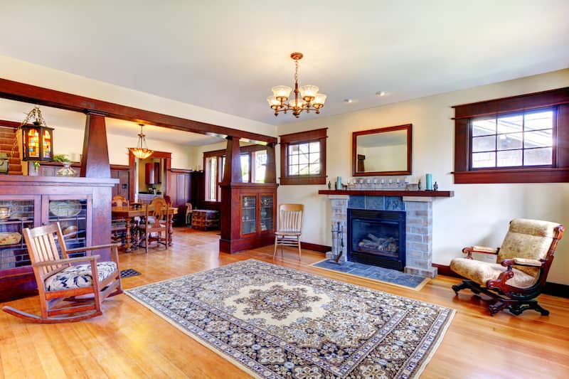 Interior of home with dark wood tapered columns, trim and paneling, light hardwood floors and an ornate area rug.