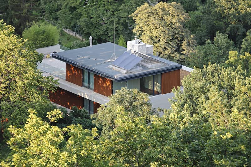 Brick red prairie style craftsman home hidden behind tree foliage and with a solar panel.