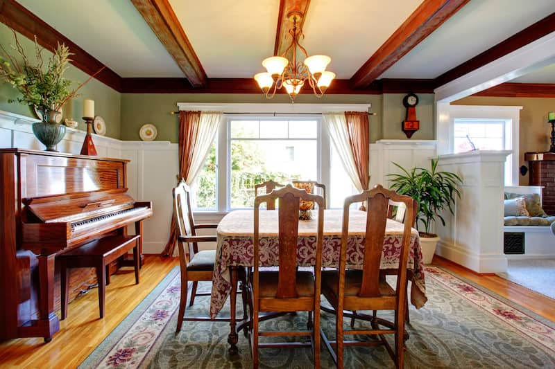 Ornate dining room with wood piano, large central window, and hanging light fixture attached to a beamed ceiling.