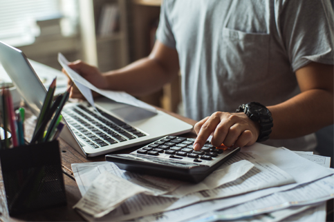 Man using calculator and reviewing documents at desk