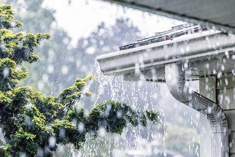Photo shows heavy rain and an overflowing gutter at the corner of a home.