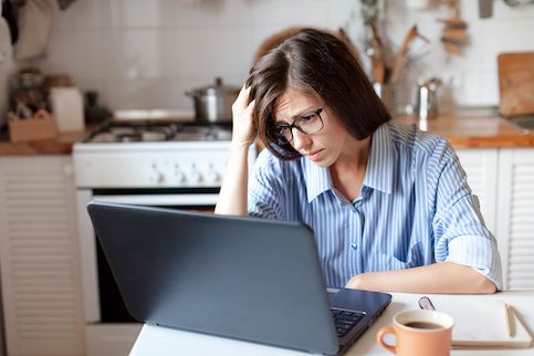 Woman in distress looking at computer with head in hand.