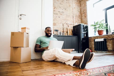 African American Man Sitting On Floor of New Apartment with Boxes