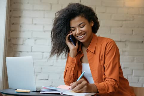 African American woman in orange shirt on phone while smiling.