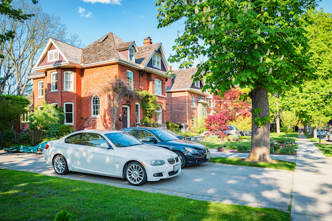 Two cars in driveway in front of a red brick home.