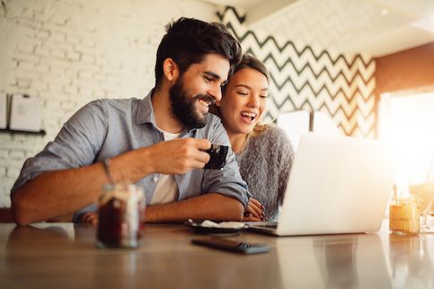 Couple drinking coffee in their kitchen and looking at laptop together.