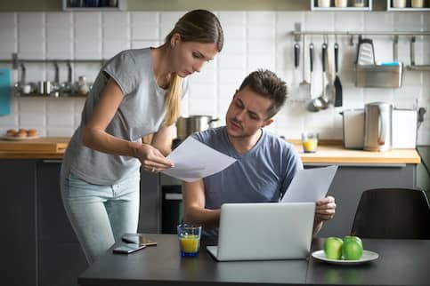 Couple in kitchen looking at documents and laptop.